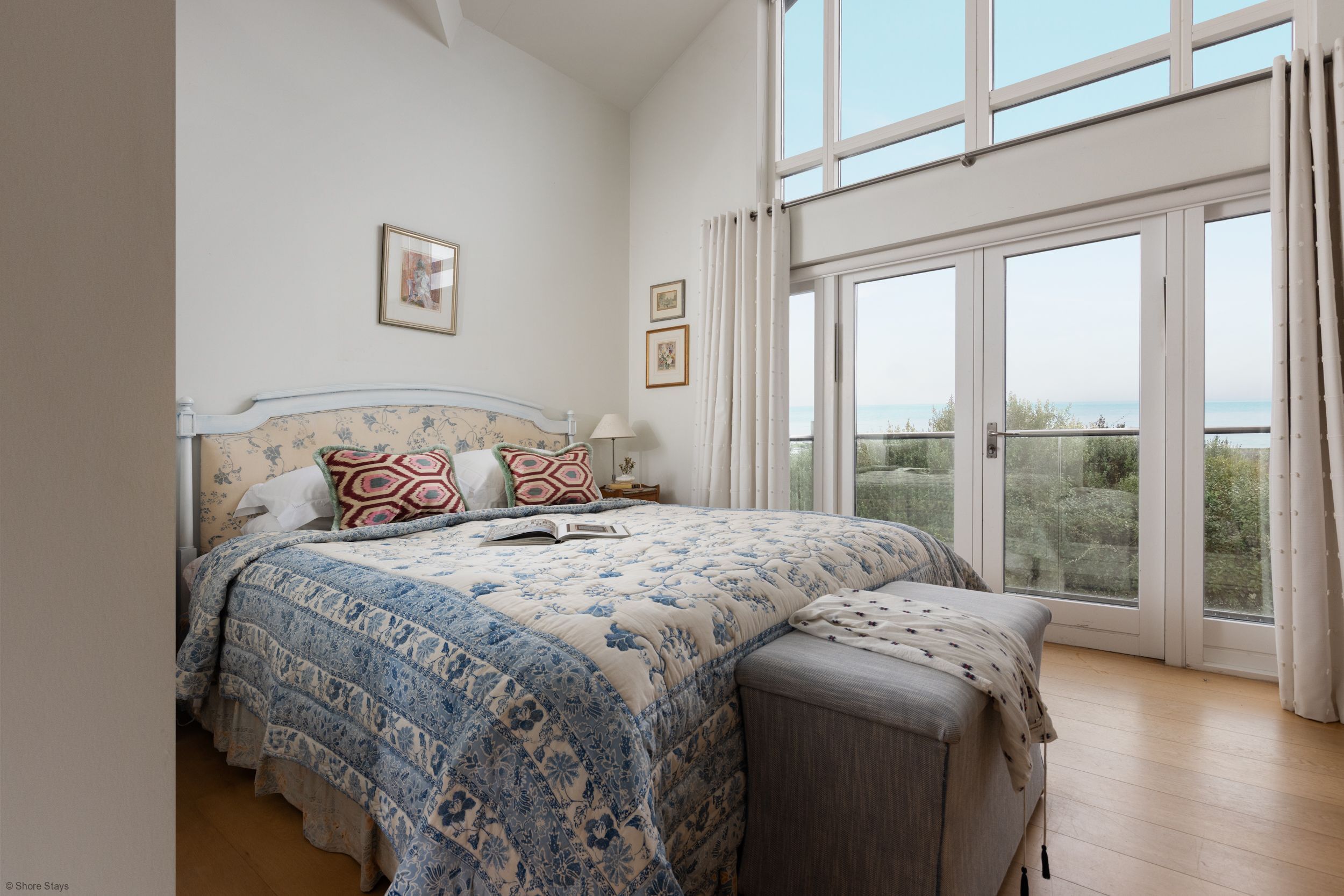 Een slaapkamer met een groot bed, een nachtkastje en uitzicht op de omgeving door een groot raam.