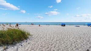 Una playa arenosa con gente y sombrillas, un cielo despejado y el océano al fondo.