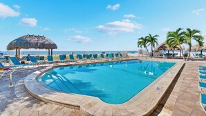 Piscina con sillas de descanso y una sombrilla de paja, rodeada de palmeras y vistas al océano.