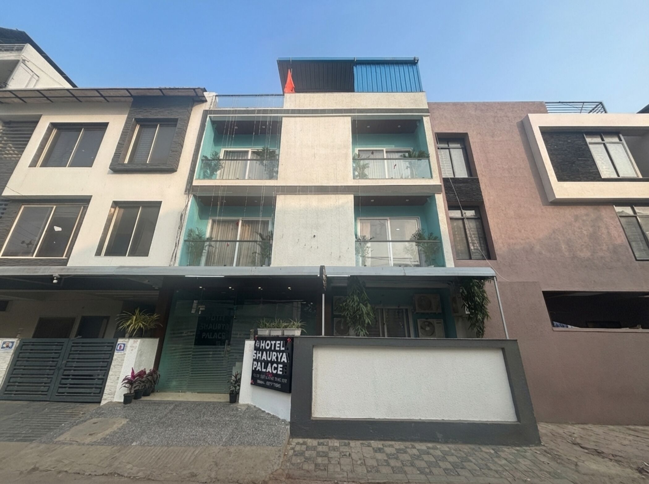 Een hotel met meerdere verdiepingen, een moderne gevel, grote ramen en een bord met de tekst Hotel Shaurya Palace.