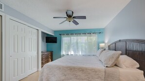 Ein Schlafzimmer mit Bett, Deckenventilator, Fernseher und einem Fenster mit Vorhängen.