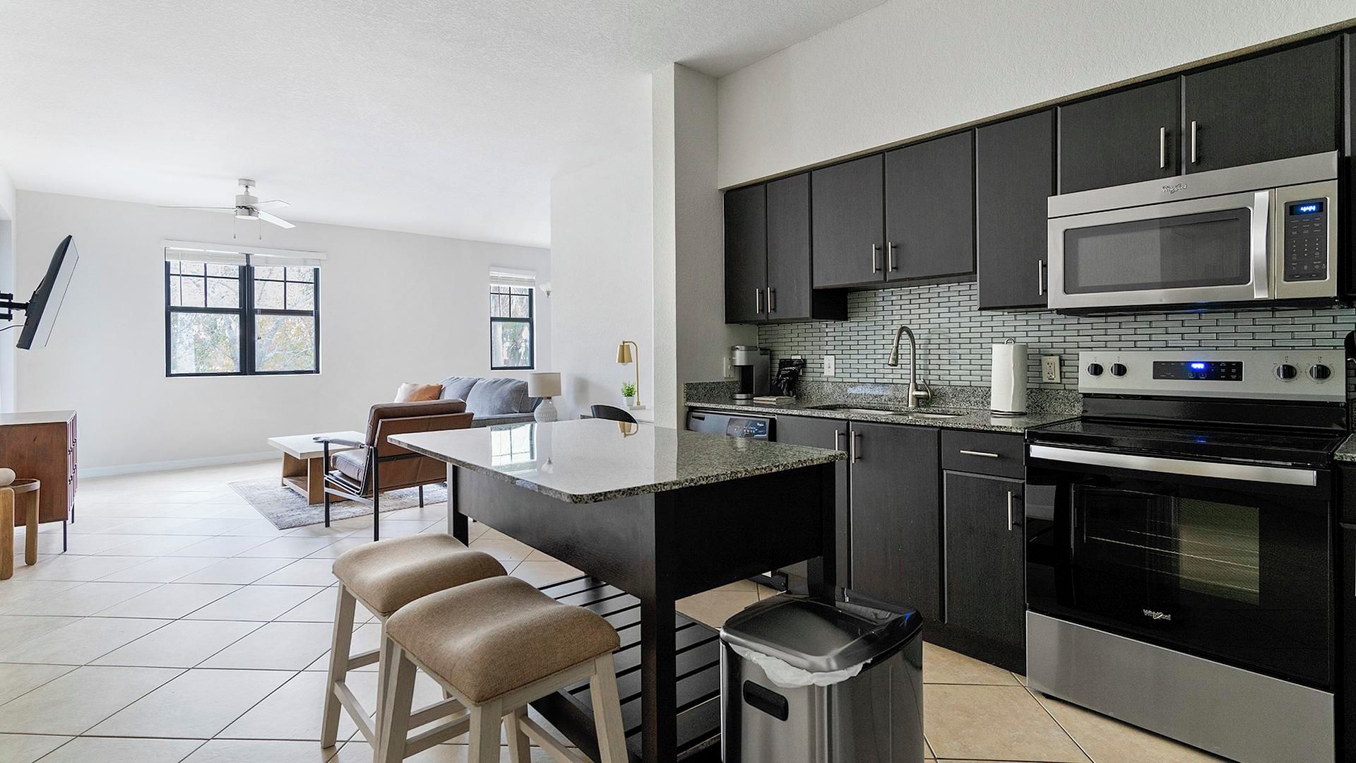 A modern kitchen with a central island, stainless steel appliances, and a dining area with a sofa and chairs.