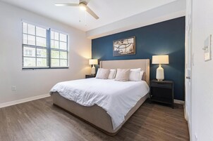 Una camera da letto con un letto grande, due comodini con lampade, una ventola a soffitto, una finestra con tende e un'opera d'arte appesa al muro.