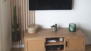 A modern living room with a flat-screen TV mounted on the wall, a wooden console table with decorative items, and a tall striped wall. - Air-conditioned studio with magnificent sea view and swimming pool (Sainte-Maxime)