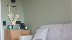 A living room with a grey sofa, wooden side table, and a wall-mounted macrame decoration. - Air-conditioned studio with magnificent sea view and swimming pool (Sainte-Maxime)