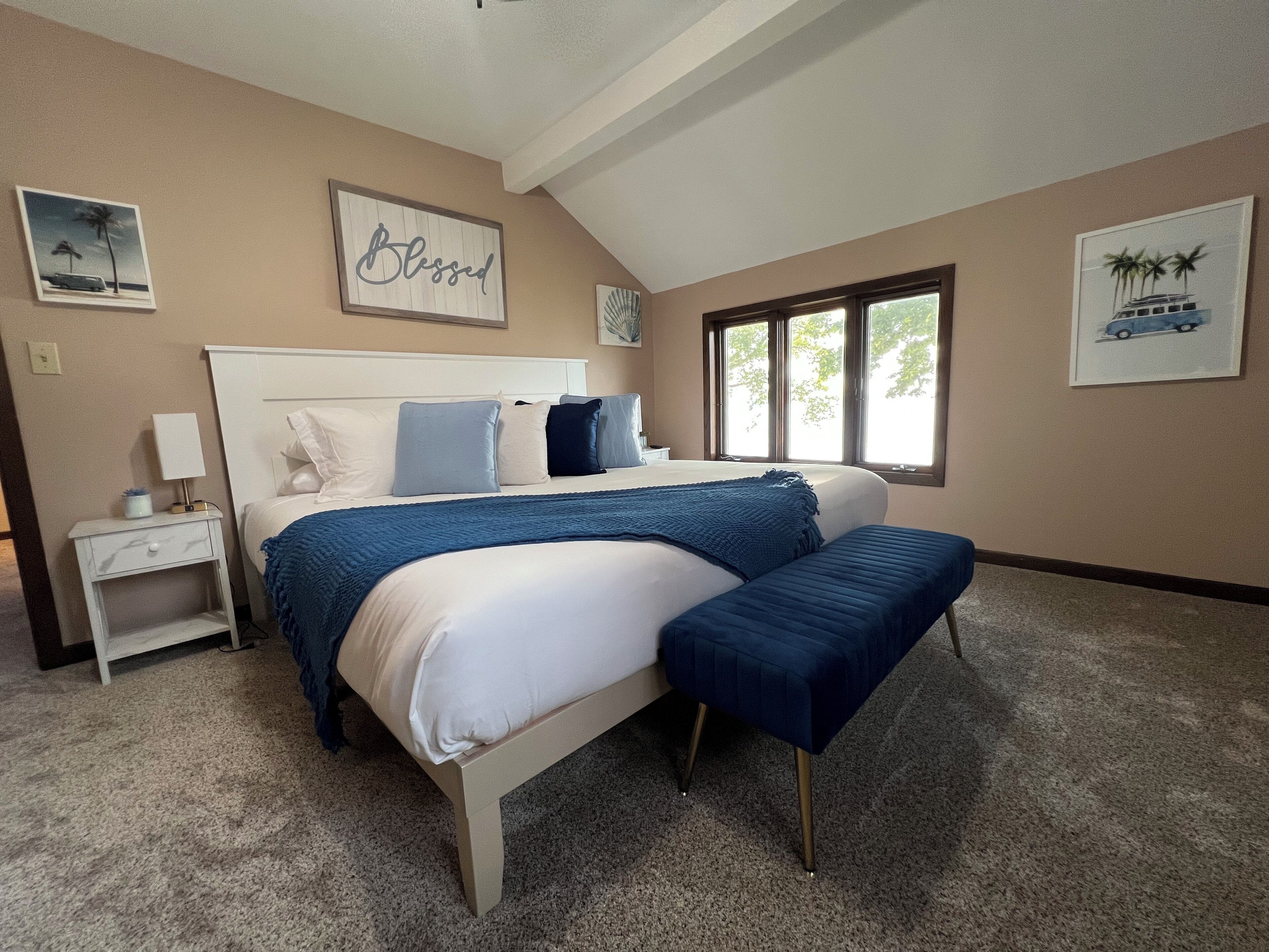Une chambre à coucher avec un grand lit, une table de chevet, une fenêtre et des œuvres d’art murales.