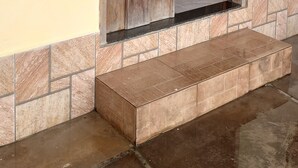 Una puerta de madera con un cerrojo metálico, un piso de baldosas y un suelo de concreto.
