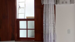 Una habitación con una silla de madera, una mesita pequeña, un ventanal con cristal satinado y un equipo de aire acondicionado blanco en la pared.
