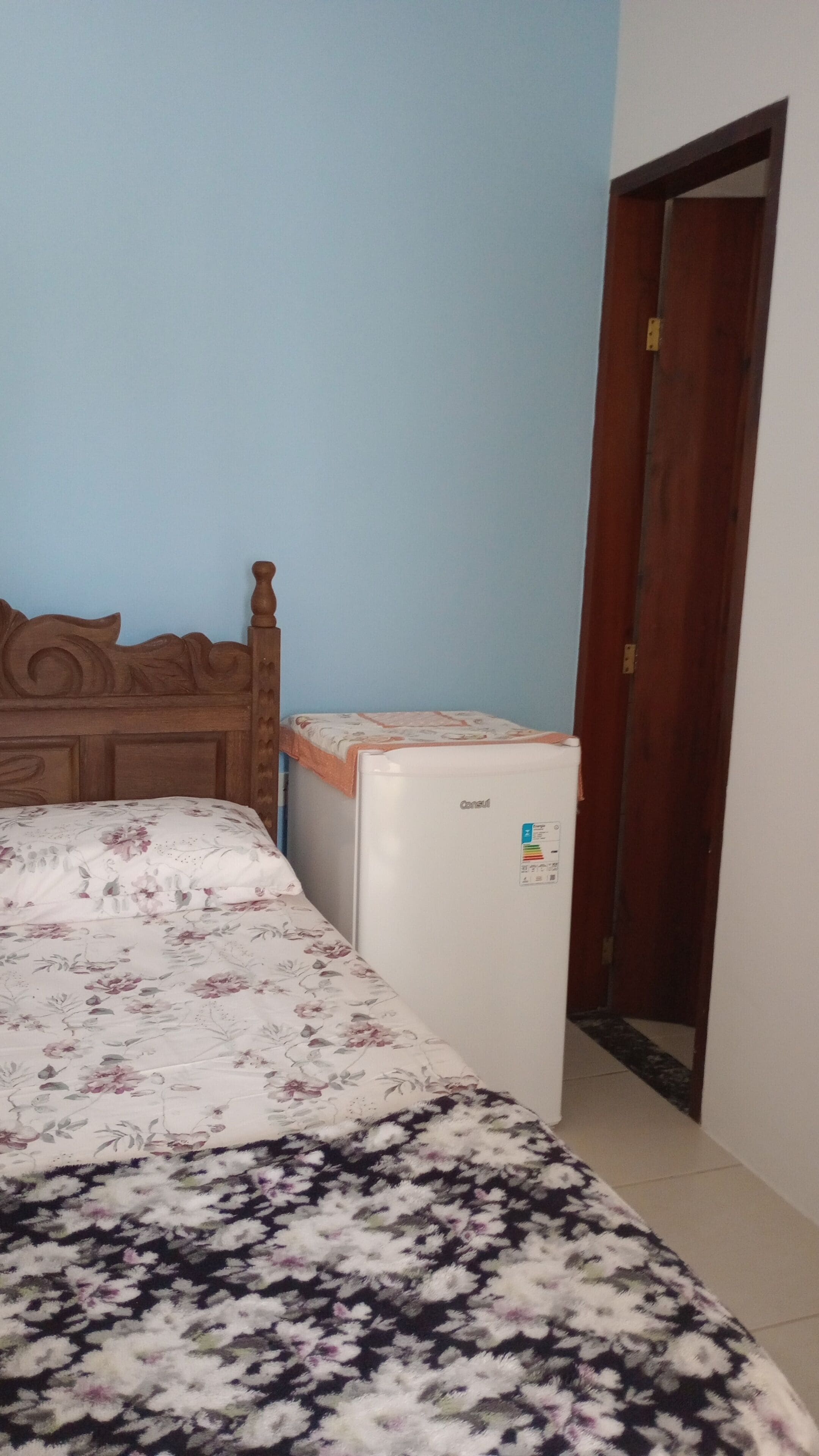Une chambre à coucher avec un lit, une tête de lit en bois, un réfrigérateur blanc et une porte.