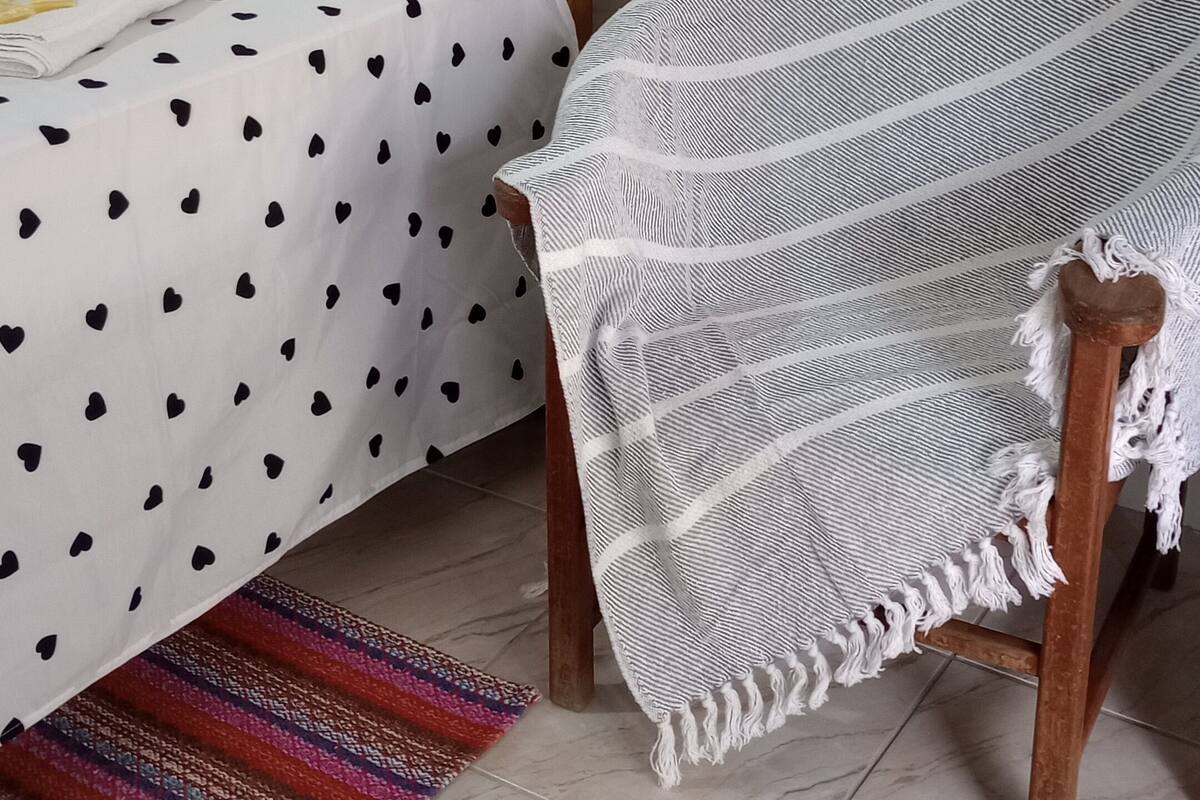 A bed with a polka dot bedspread, a white throw blanket, and a colorful woven rug.