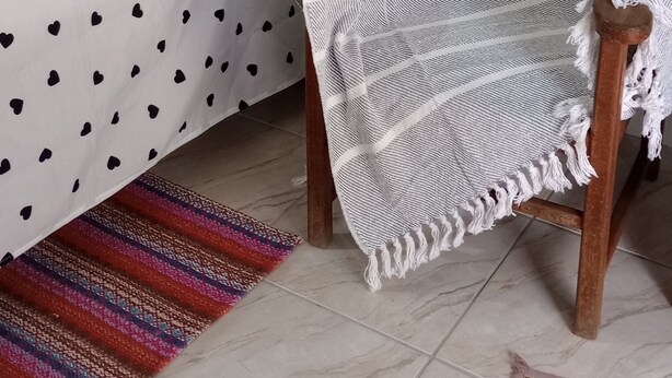 Una cama con una colcha de lunares, un plaid blanco y un tapiz tejido de colores.