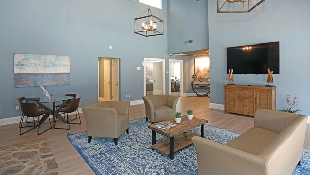 Ein geräumiges Wohnzimmer mit großem Fernseher, bequemen Sitzmöglichkeiten und einem blauen Teppich mit Muster.