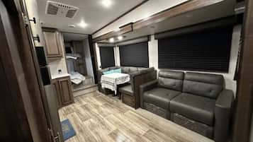 A compact RV interior with a kitchenette, a seating area with a sofa, and a table.