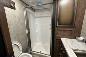 Une petite salle de bain comprenant une douche, des toilettes et un meuble-lavabo avec un évier.
