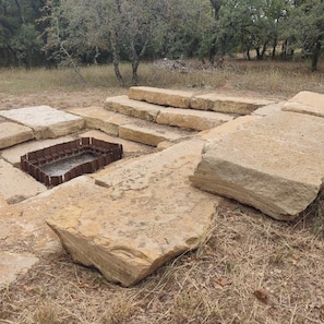 A stone structure with steps and a rectangular opening, surrounded by dry grass and trees. - 8 Hico Glamping Petting Zoo Campfire Fossil Rim (Hico)