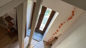 Visão através de uma porta para um quarto com piso de madeira, uma prateleira com objetos e uma parede com folhas de outono.