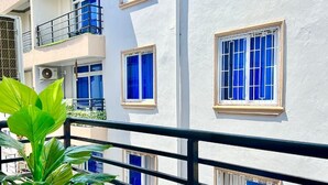 Un edificio blanco con múltiples ventanas, algunas con cortinas azules, y un balcón con barandilla negra.