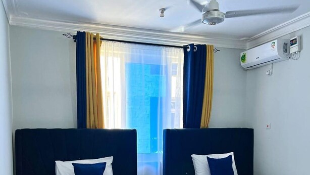 Habitación de hotel con dos camas, ventilador de techo, aire acondicionado y ventana con cortinas.