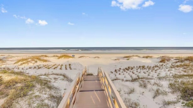 Una passerella in legno che conduce a una spiaggia con dune di sabbia e vegetazione rada.
