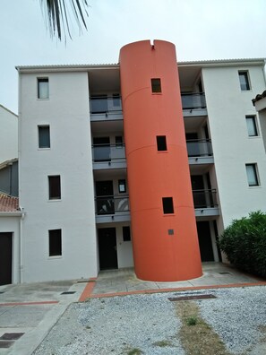 A multi-story building with a distinctive orange cylindrical structure in the center. - T2 30m2 top floor 3 to 4 sleeps quiet residence (Le Barcarès)