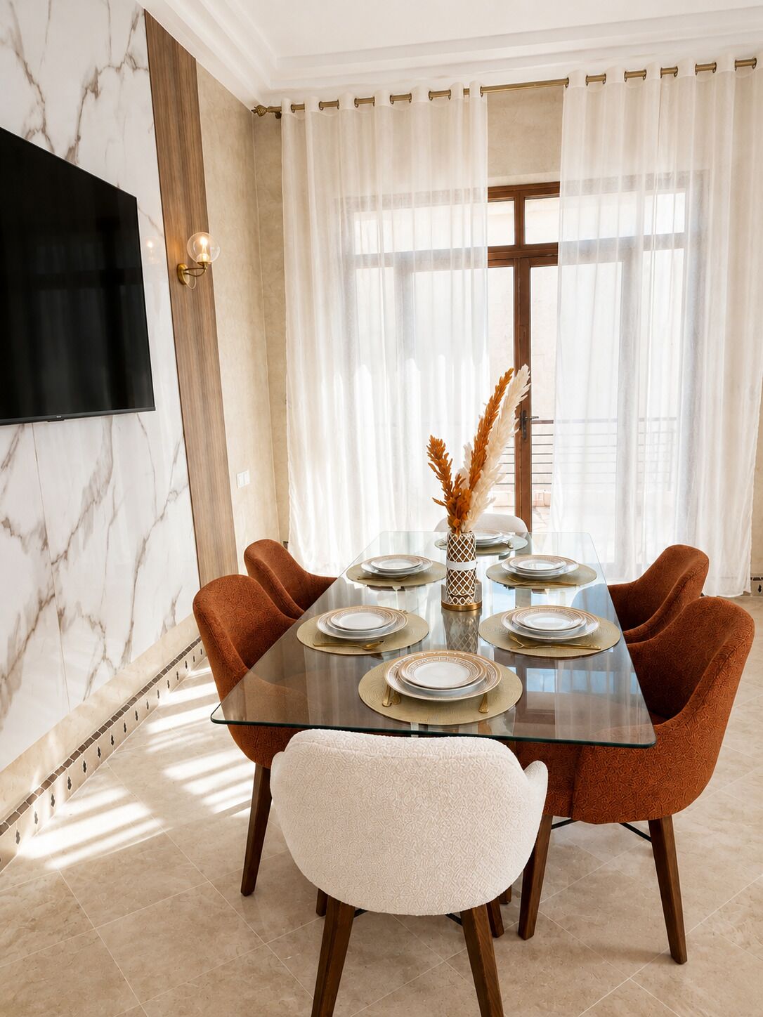 A dining area with a glass table, six chairs, and a TV mounted on the wall.