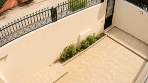 Ein Balkon mit Fliesenboden, schwarzem schmiedeeisernen Geländer und einem kleinen Gartenbereich mit Pflanzen.