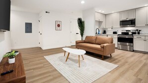 Un salon moderne avec un canapé marron, une table basse blanche et une table d’appoint en bois sur laquelle est posée une plante.