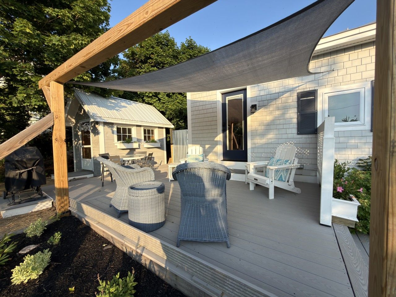 Una terrazza coperta con mobili da esterno, un barbecue e una casa sullo sfondo.