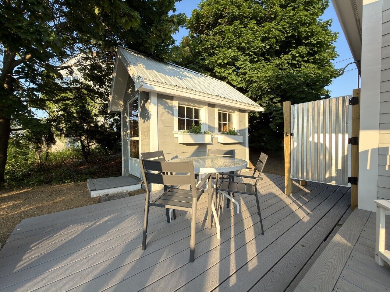 A wooden deck with a table and chairs, a small house with a metal roof, and a wooden fence.