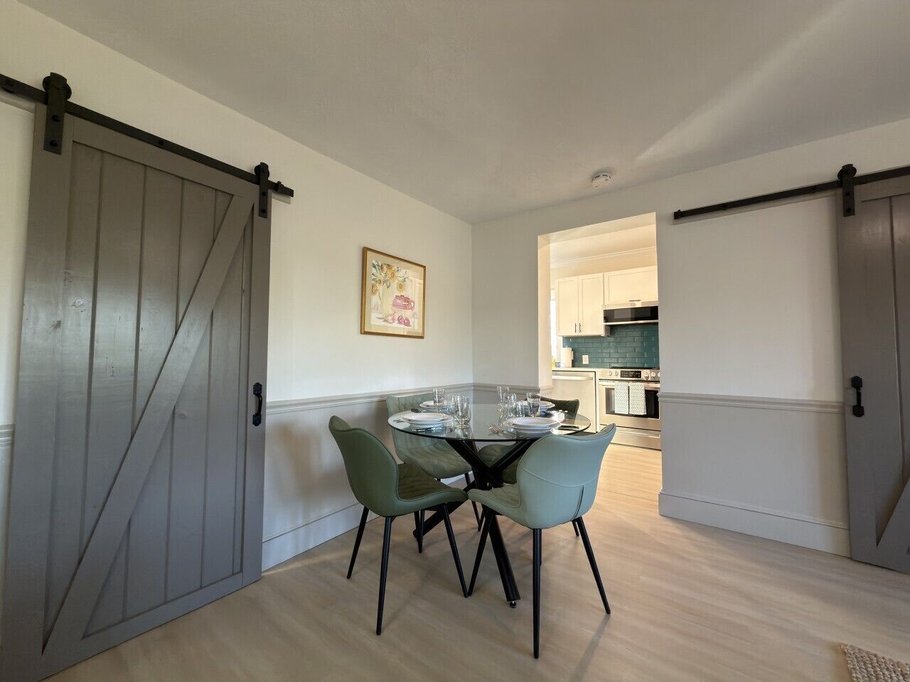 Un comedor con una mesa de vidrio, cuatro sillas y una puerta corredera de estilo rústico.