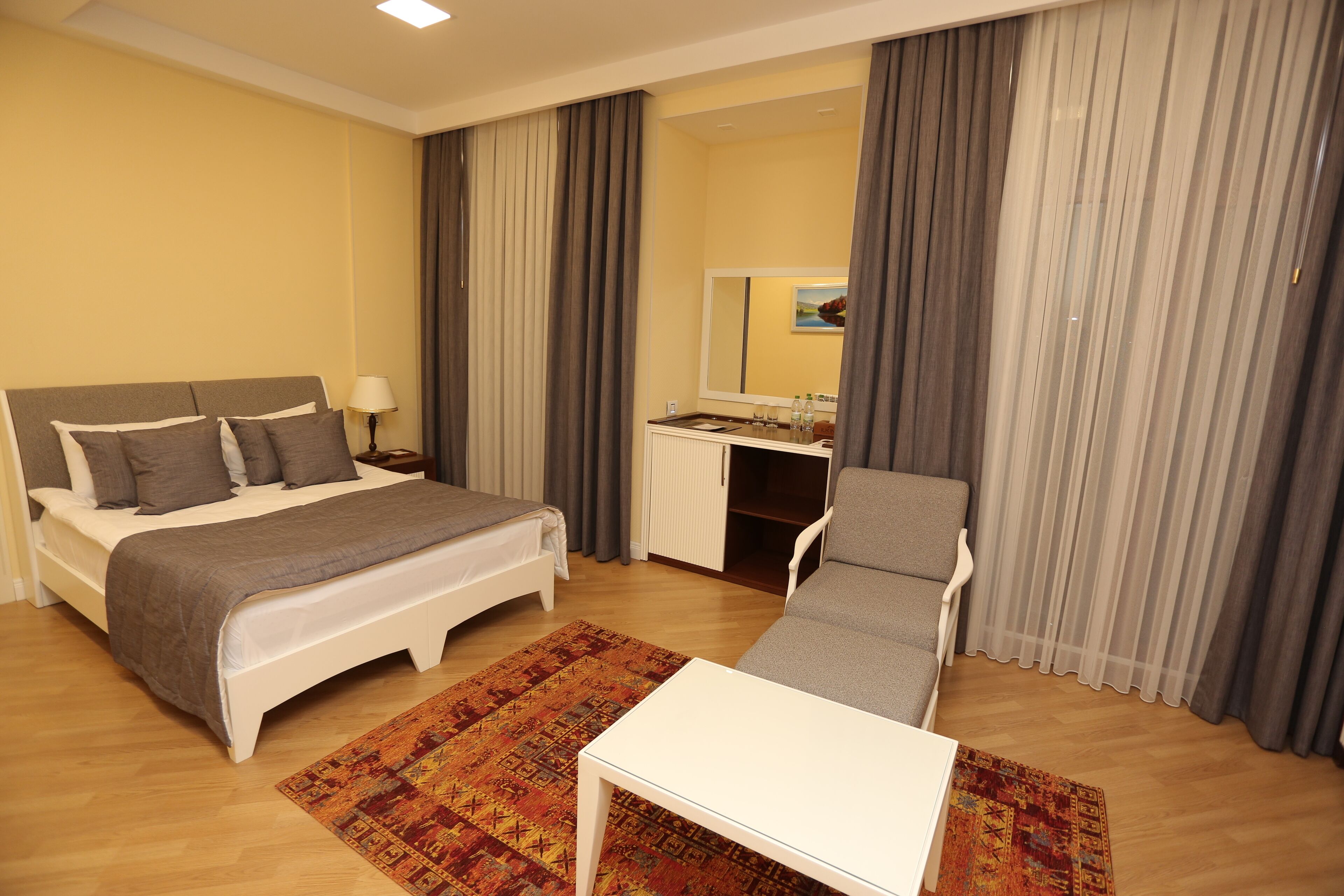Hotellihuone, jossa on sänky, työpöytä, tuoli, pieni pöytä ja peili.