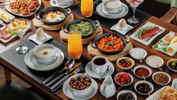 A dining table set with a variety of breakfast dishes, including eggs, pancakes, and a fruit salad. - ILK INN HOTEL (Qusar)