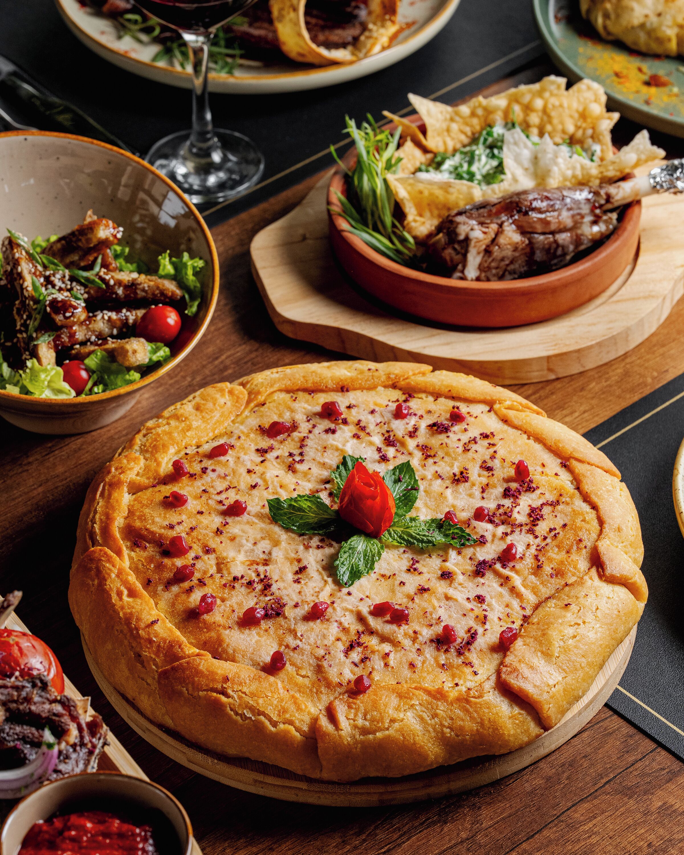 A variety of dishes including a pizza with a rose garnish, a bowl of salad, and a plate with meat.