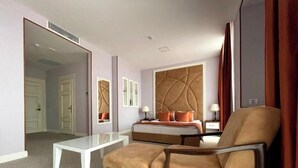 A hotel room with a bed, a sitting area with a chair and a table, a mirror, and a door leading to another room. - ILK INN HOTEL (Qusar)