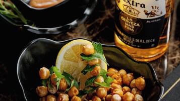 Un tazón de garbanzos adornado con perejil y limón, con una botella de cerveza Corona Extra al fondo.
