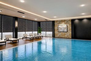 Una piscina con sillas de descanso, una pared de piedra con obras de arte e iluminación empotrada en el techo.
