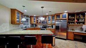 Una cocina moderna con encimeras de granito, electrodomésticos de acero inoxidable, armarios de madera y una barra con taburetes.