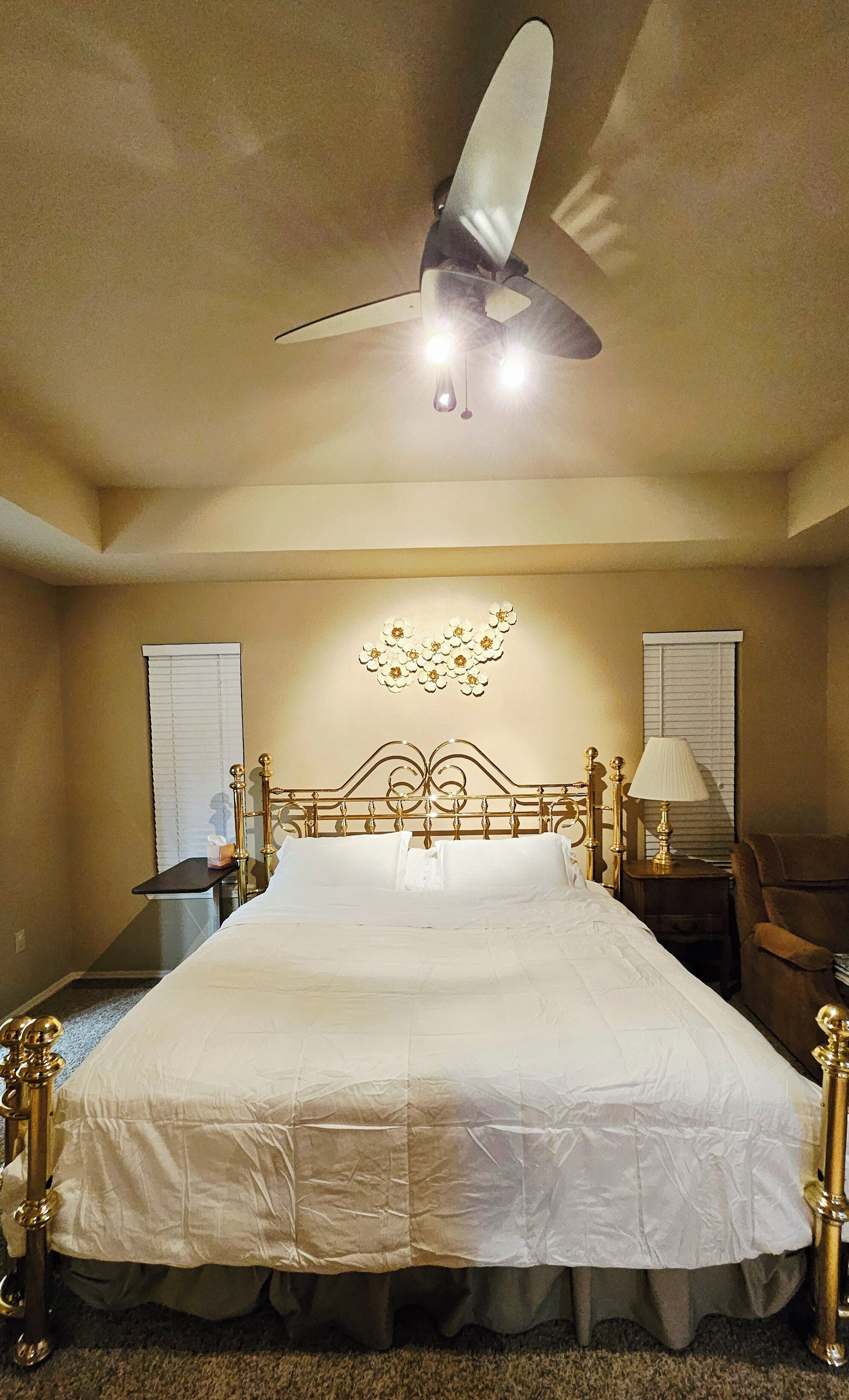Une chambre avec un grand lit, un ventilateur de plafond et un élément décoratif mural.