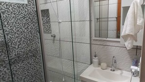 Une salle de bain avec une douche à parois de verre, un lavabo blanc avec un miroir et une serviette accrochée au mur.