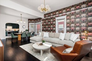 A modern living room with a sofa, coffee table, and chairs. There is a dining area with a table and chairs. The room has a large window and a floral wallpaper. - The Wild Peony | Walk to Old Town FC & CSU Campus (Fort Collins)