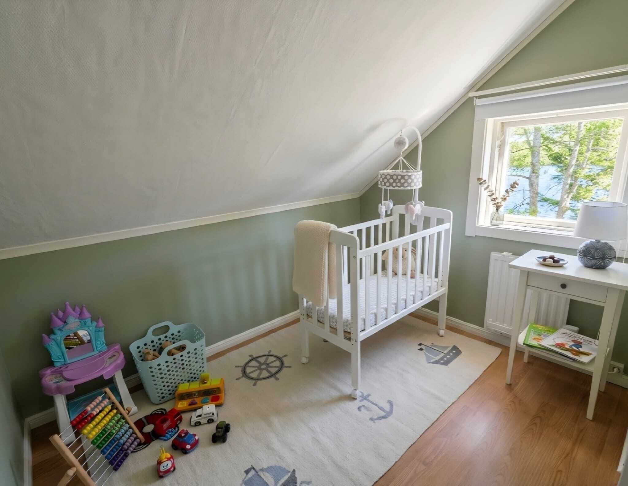 Una habitación infantil con una cuna, juguetes, un ventanal y un pequeño escritorio con lámpara.