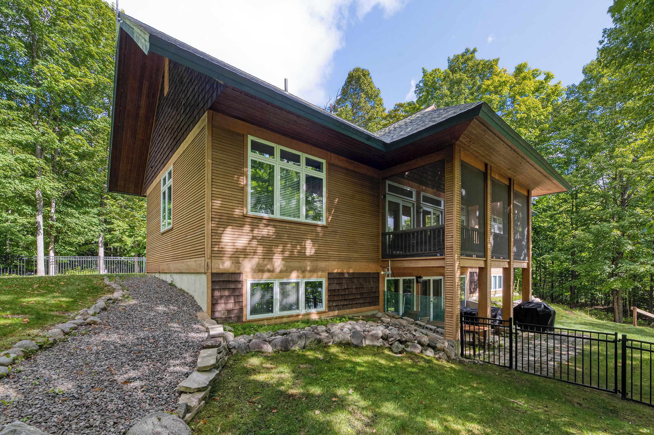 A two-story house with a stone foundation, wooden siding, and large windows.