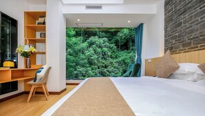 Une chambre d’hôtel moderne dotée d’un grand lit, d’un bureau avec une chaise, d’une bibliothèque et offrant une vue sur une forêt grâce à une grande fenêtre.