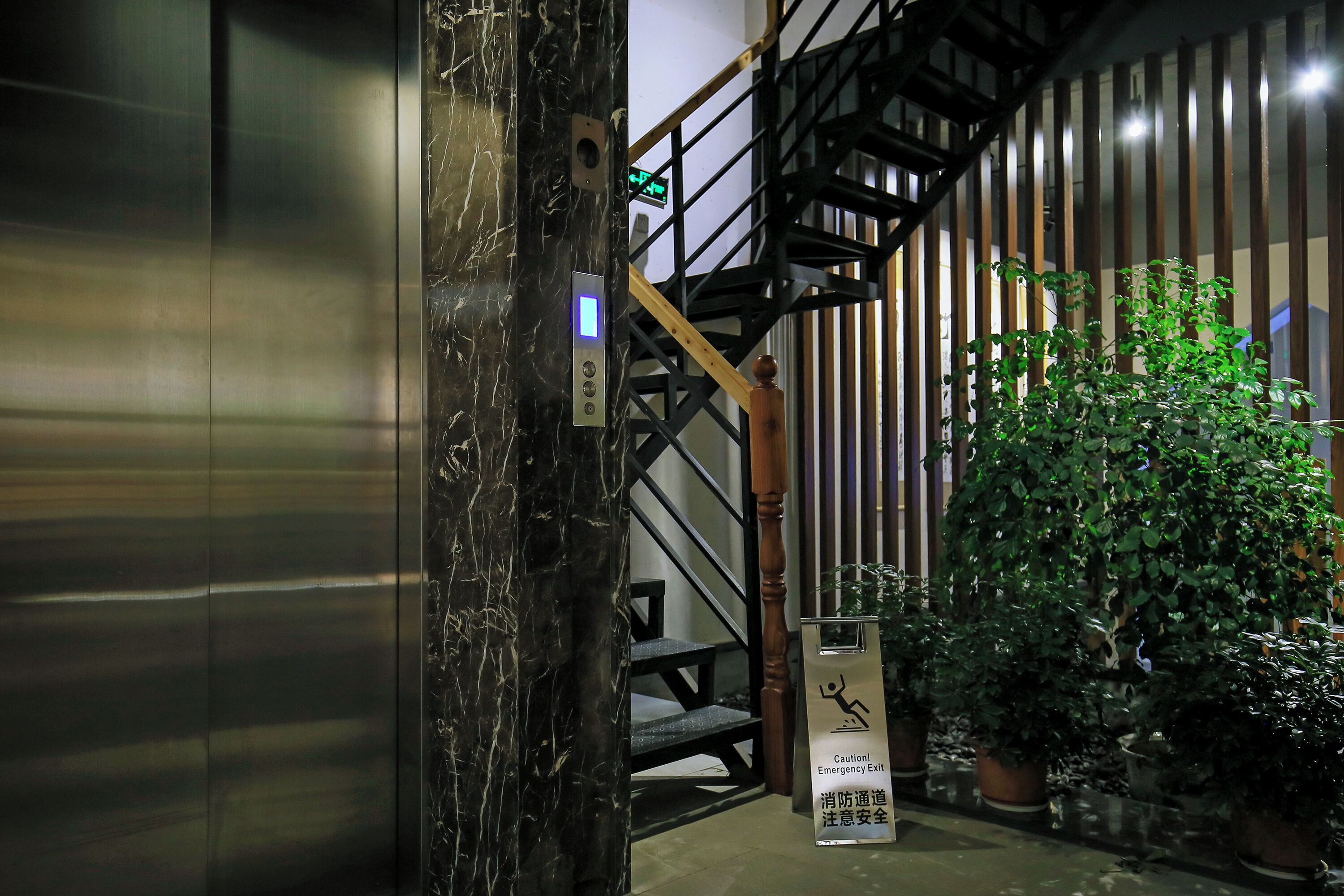 A staircase with a caution sign, emergency exit sign, and potted plants.