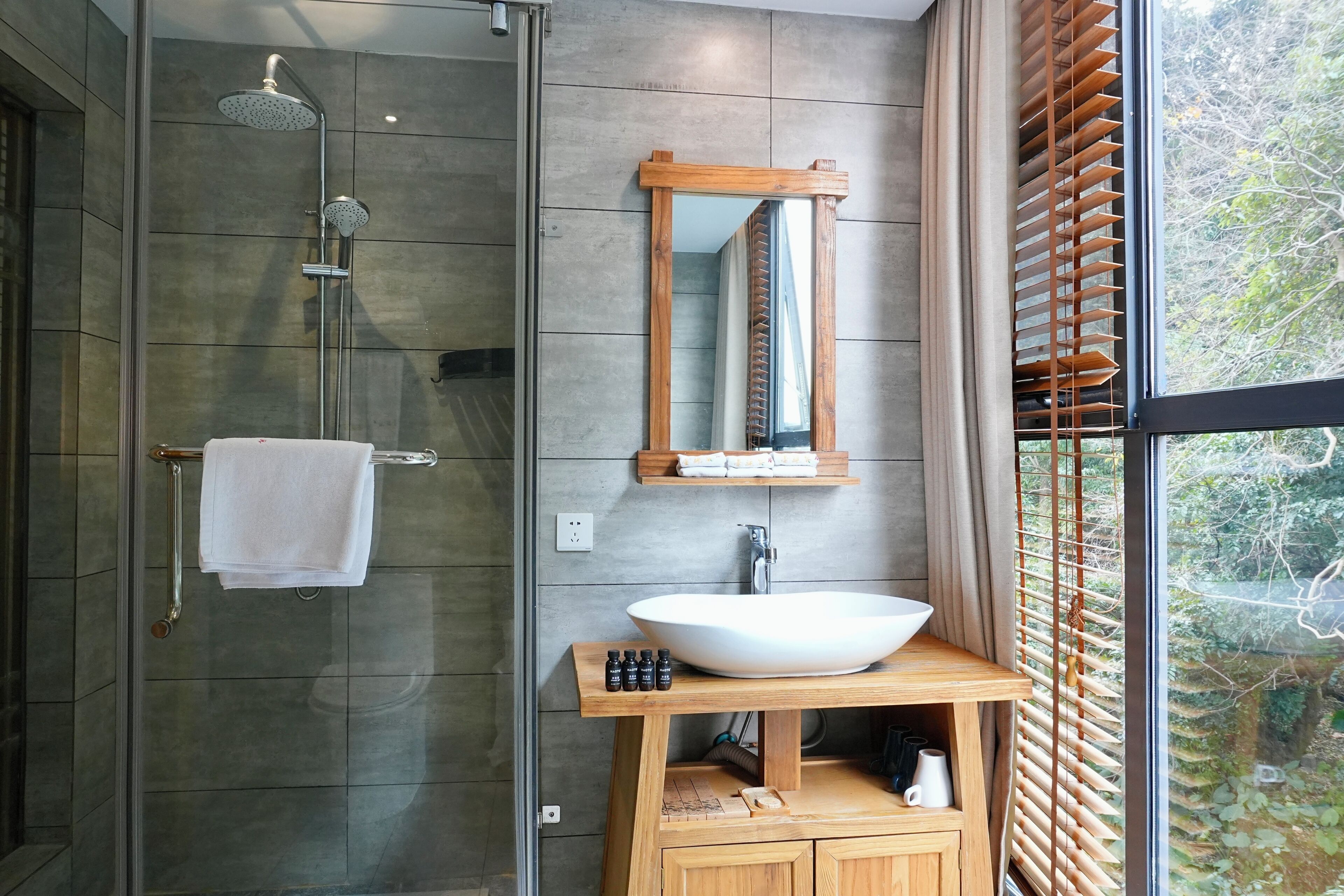 A modern bathroom with a glass shower enclosure, a large white sink, and a wooden vanity.