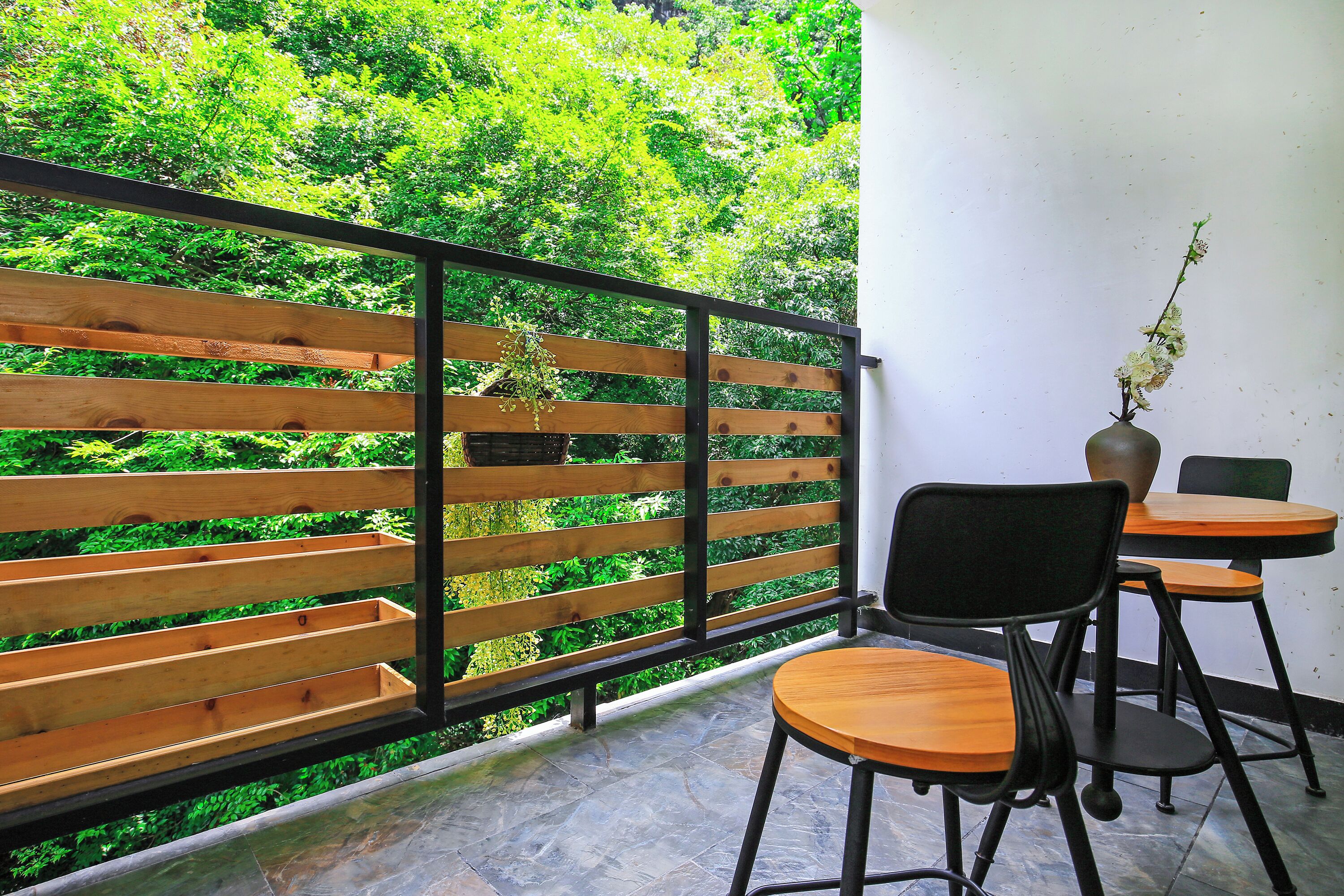 A balcony with a wooden railing, a table with a vase, and a chair.