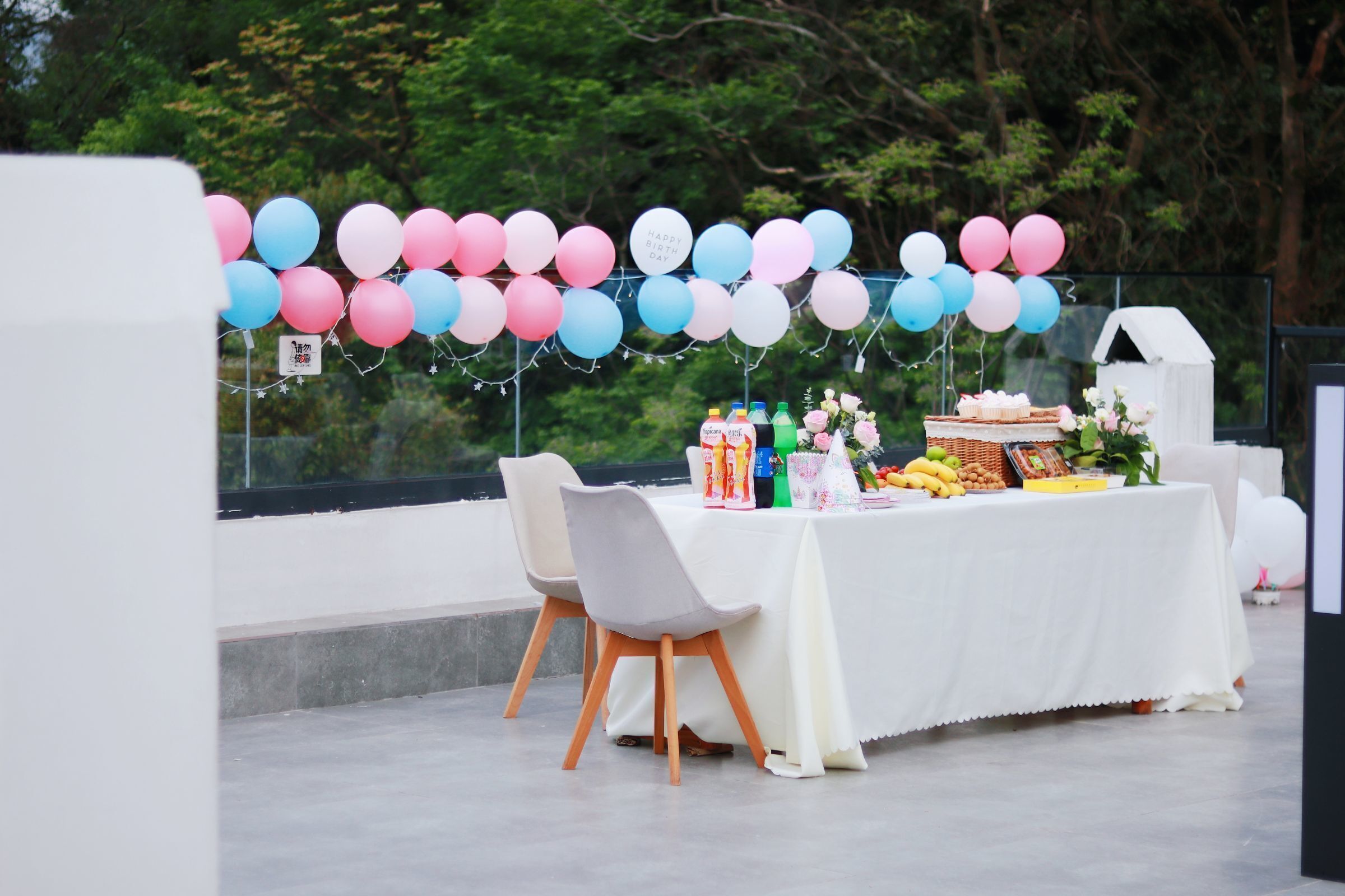 Mesa al aire libre decorada con globos, mantel blanco y diferentes platillos.