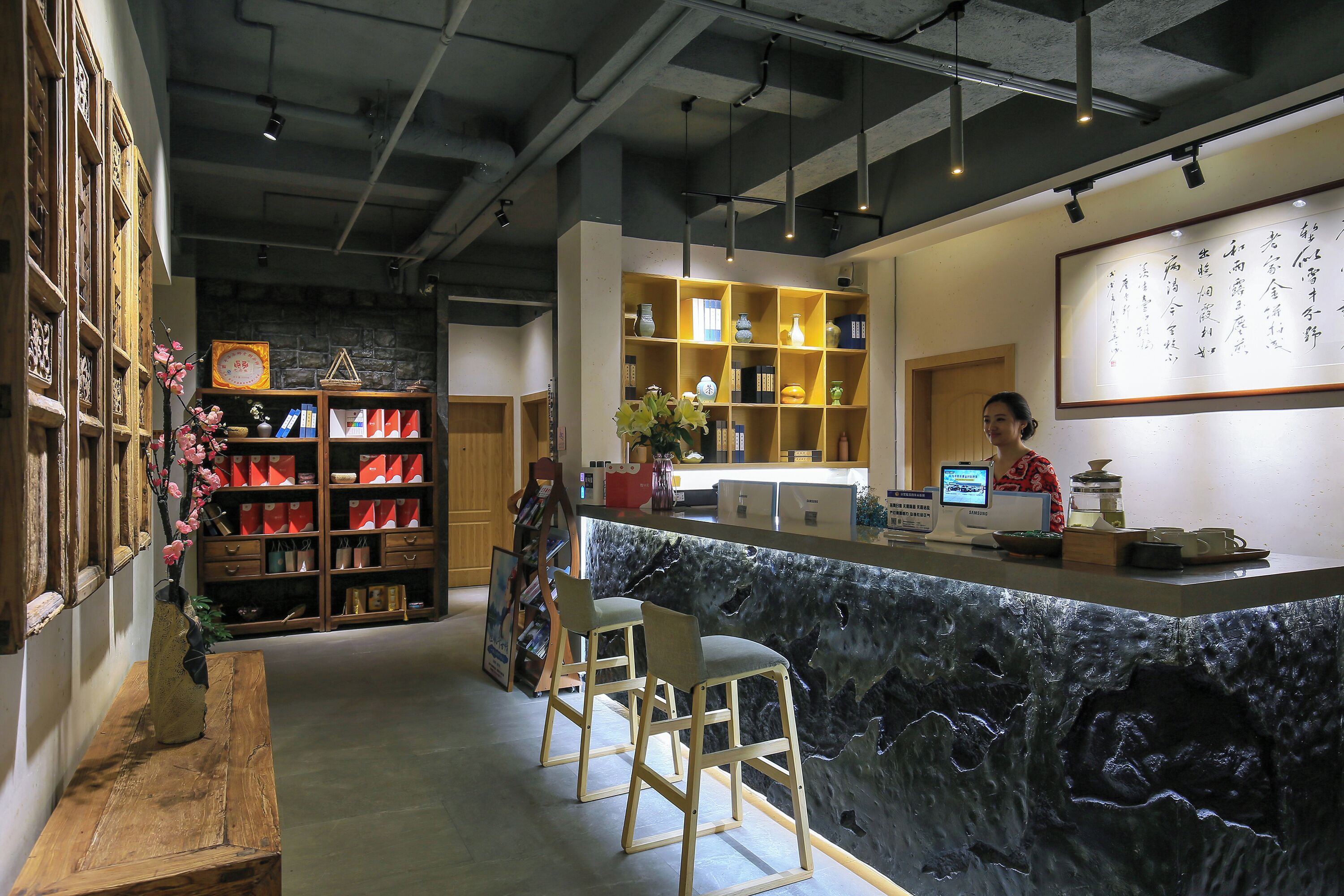 Un espace d’accueil doté d’un comptoir en pierre, d’étagères en bois et d’une grande œuvre calligraphique accrochée au mur.