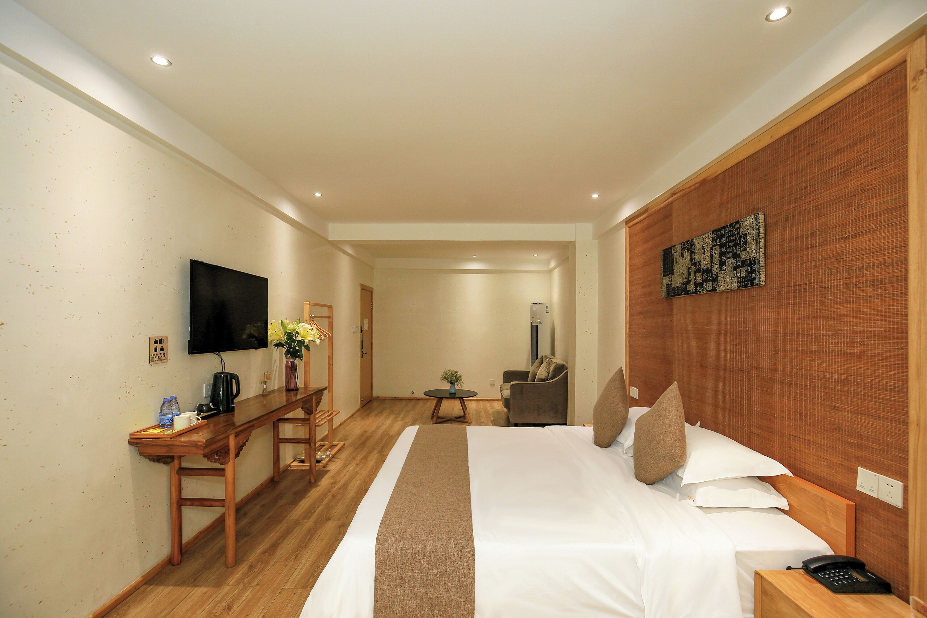 Una habitación de hotel con una cama, un escritorio, una silla, un televisor y una mesita con un florero.