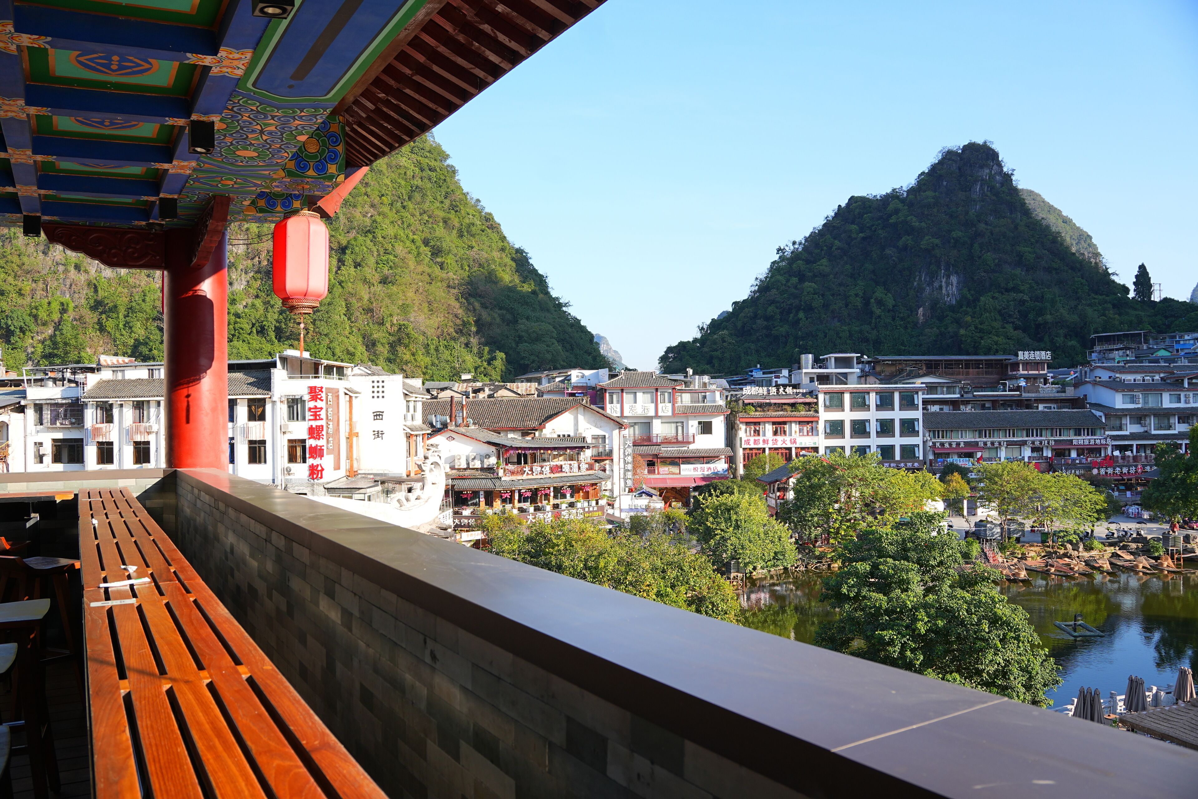 A traditional building with a wooden bench, a river, and a mountain in the background.